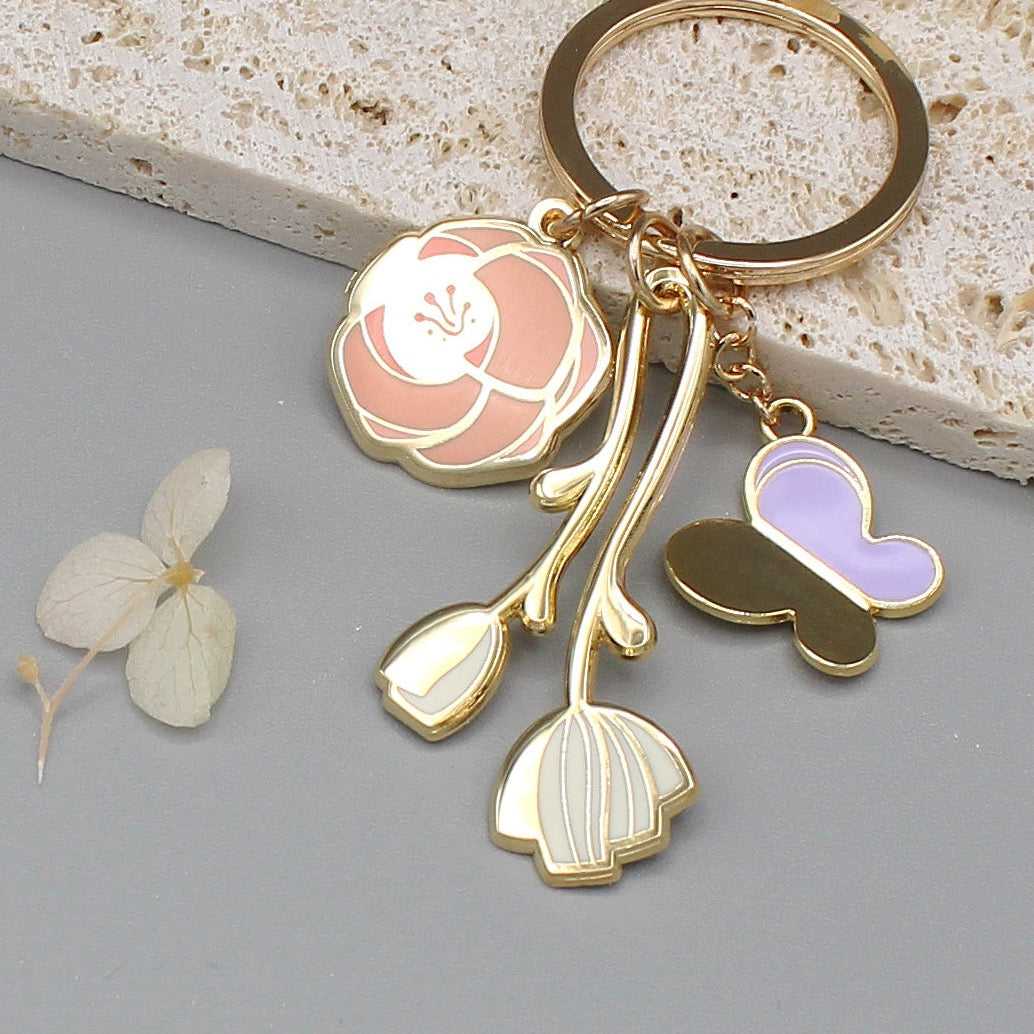 Gold plated minimal garden keychain featuring rose, peony, and butterfly charms on a gray background.