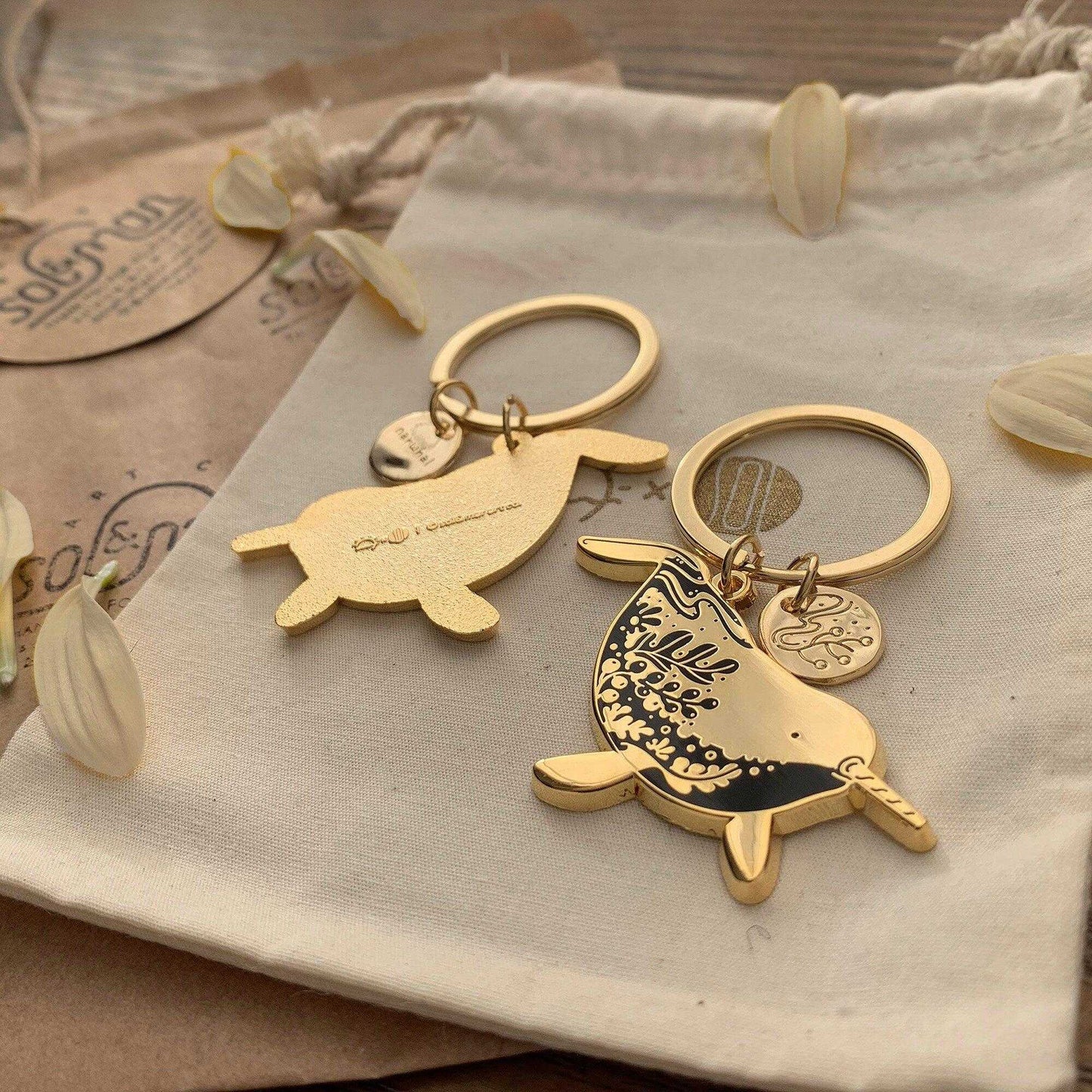 Narwhal enamel keychain set on a natural fabric background, promoting endangered animals awareness.