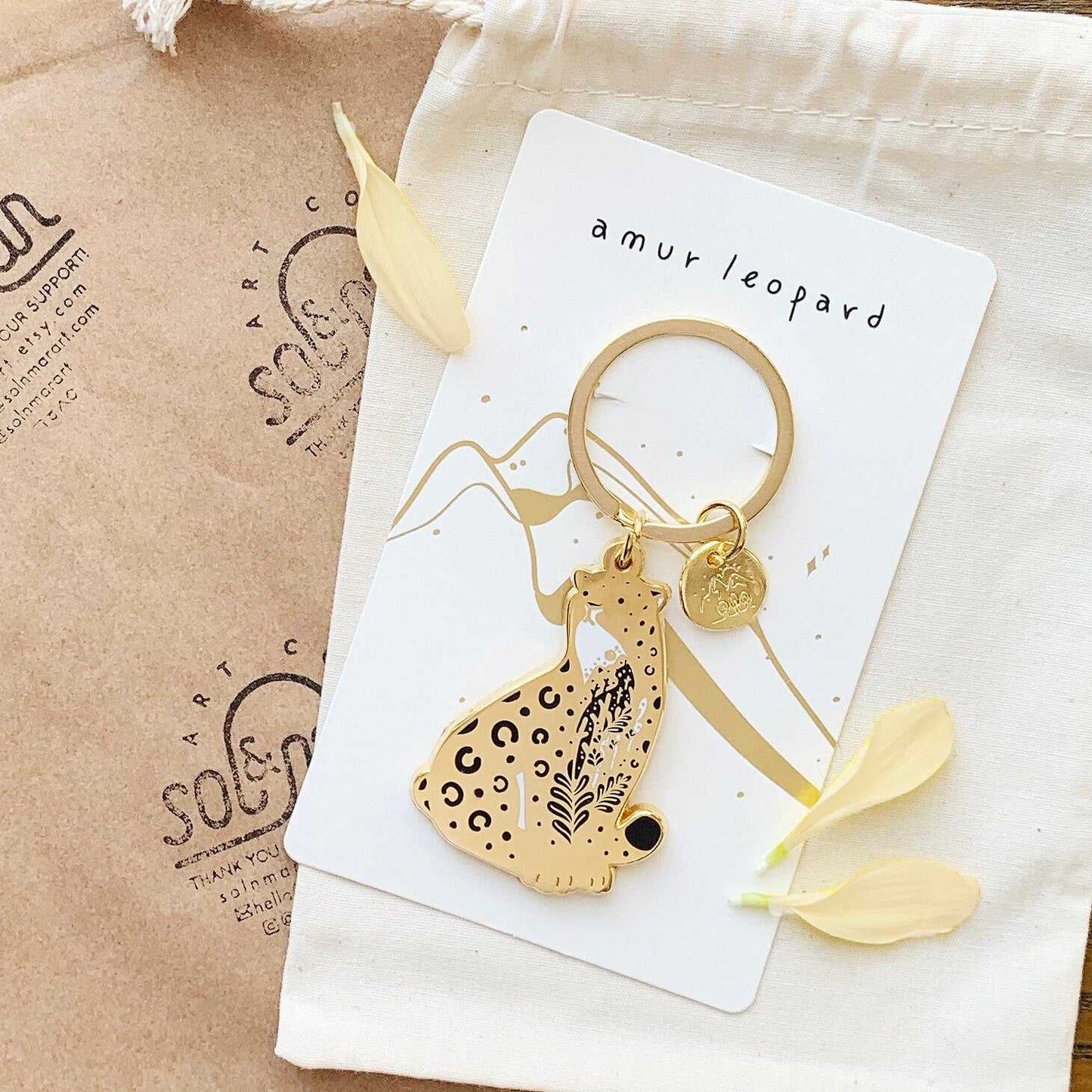 Amur leopard enamel keychain with habitat design on display card for endangered animal awareness.