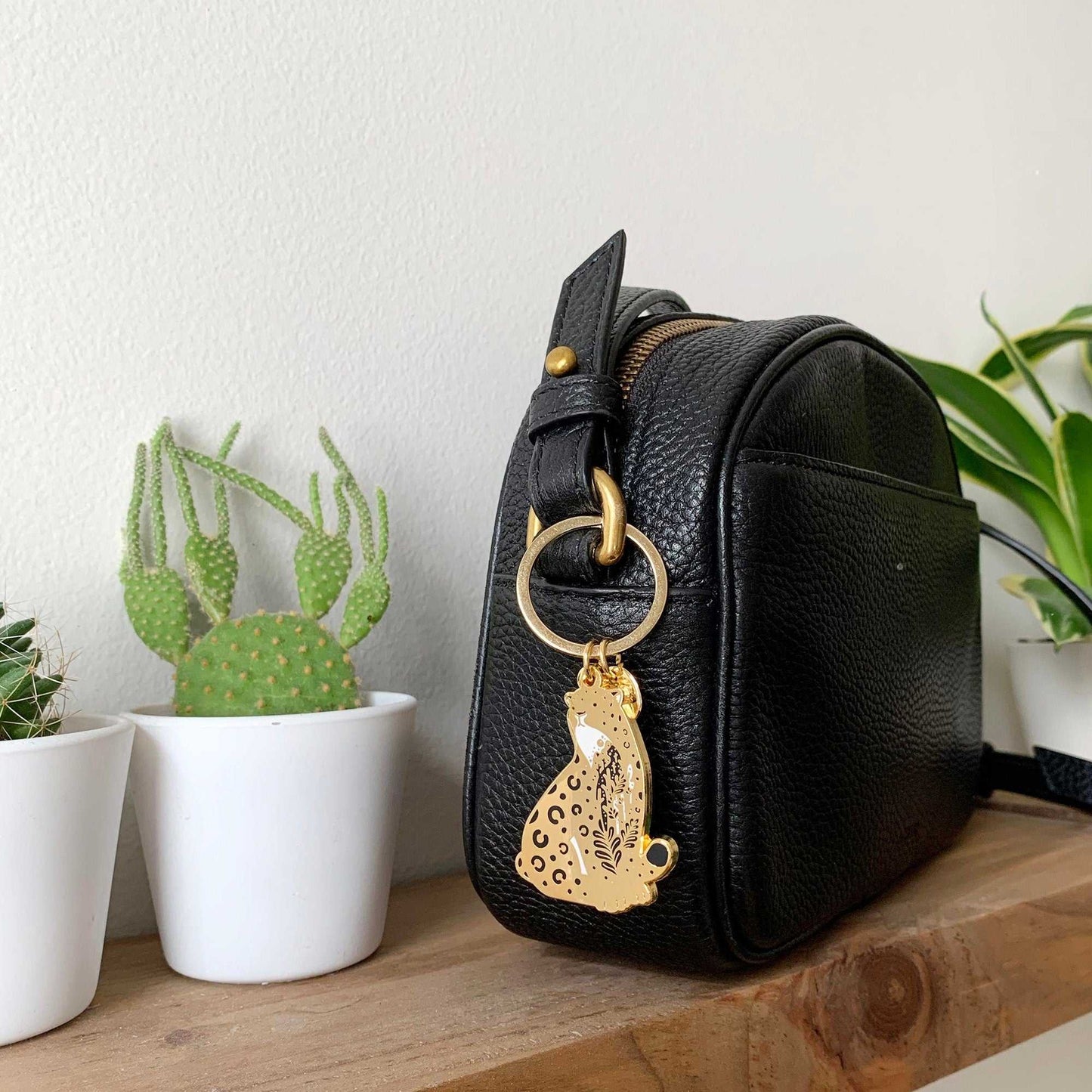 Leopard enamel keychain attached to a black bag, alongside small potted cacti.