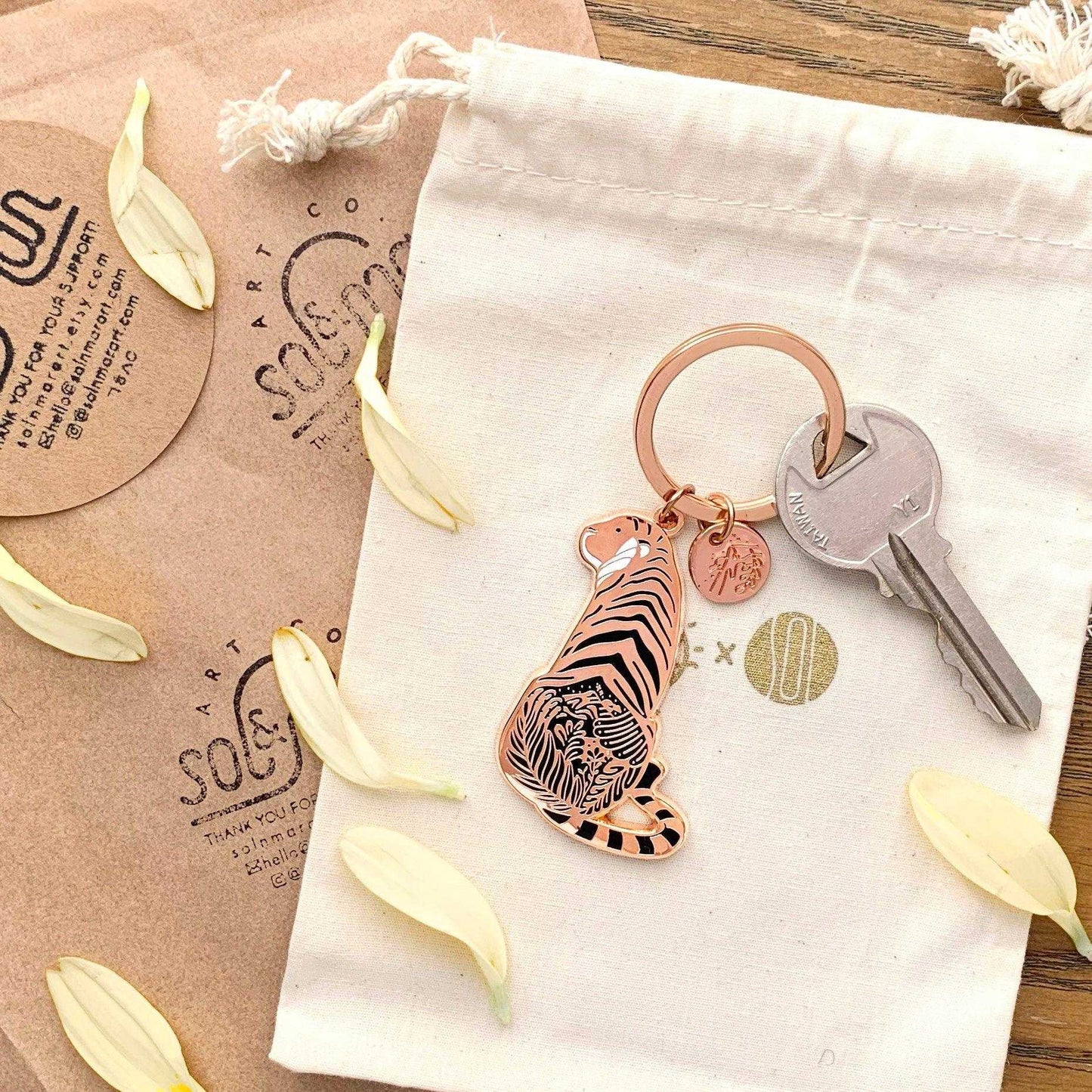 Sunda Tiger enamel keychain displayed on a soft pouch with floral accents, promoting awareness for endangered species.