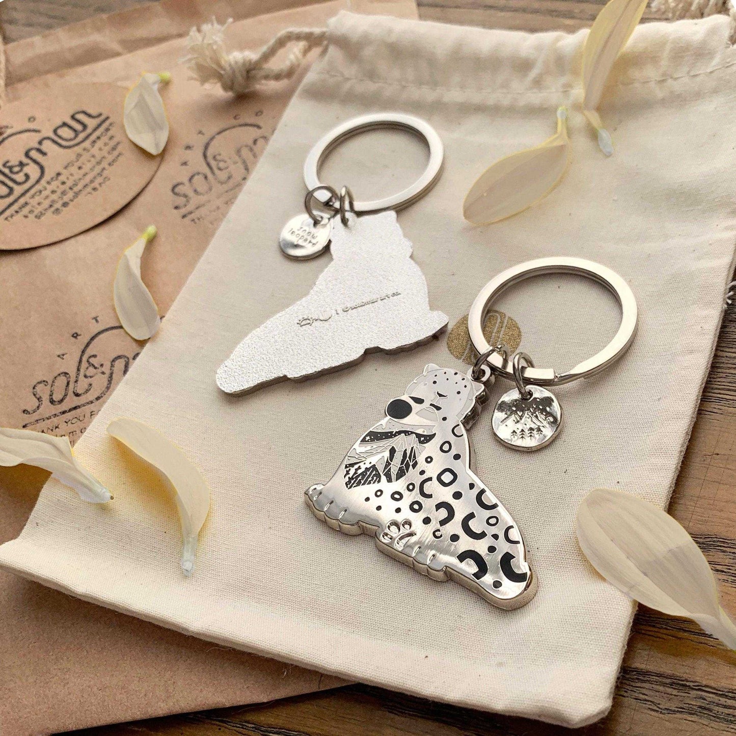 Snow Leopard enamel keychain featuring delicate habitat art, eco-friendly design, and a tag for endangered species awareness.