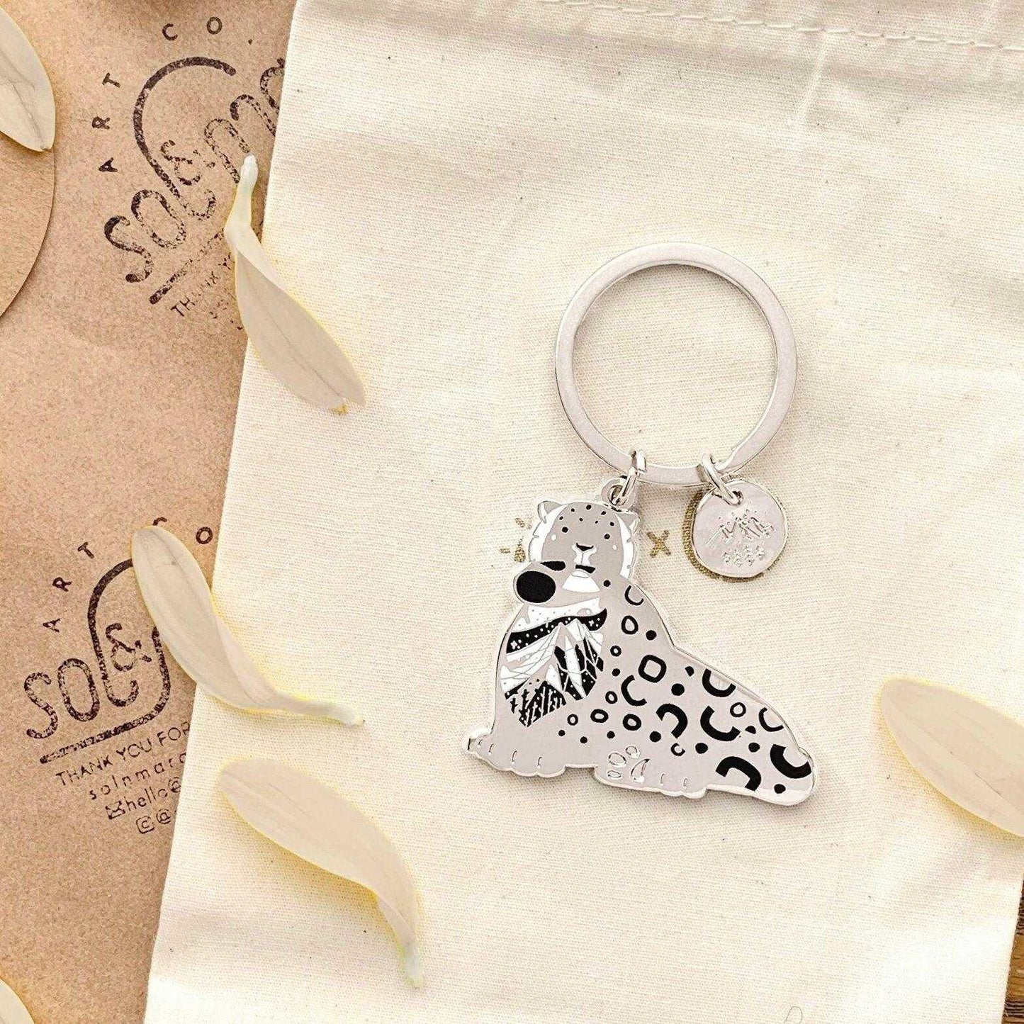 Snow Leopard enamel keychain featuring detailed art and habitat design, promoting wildlife conservation.