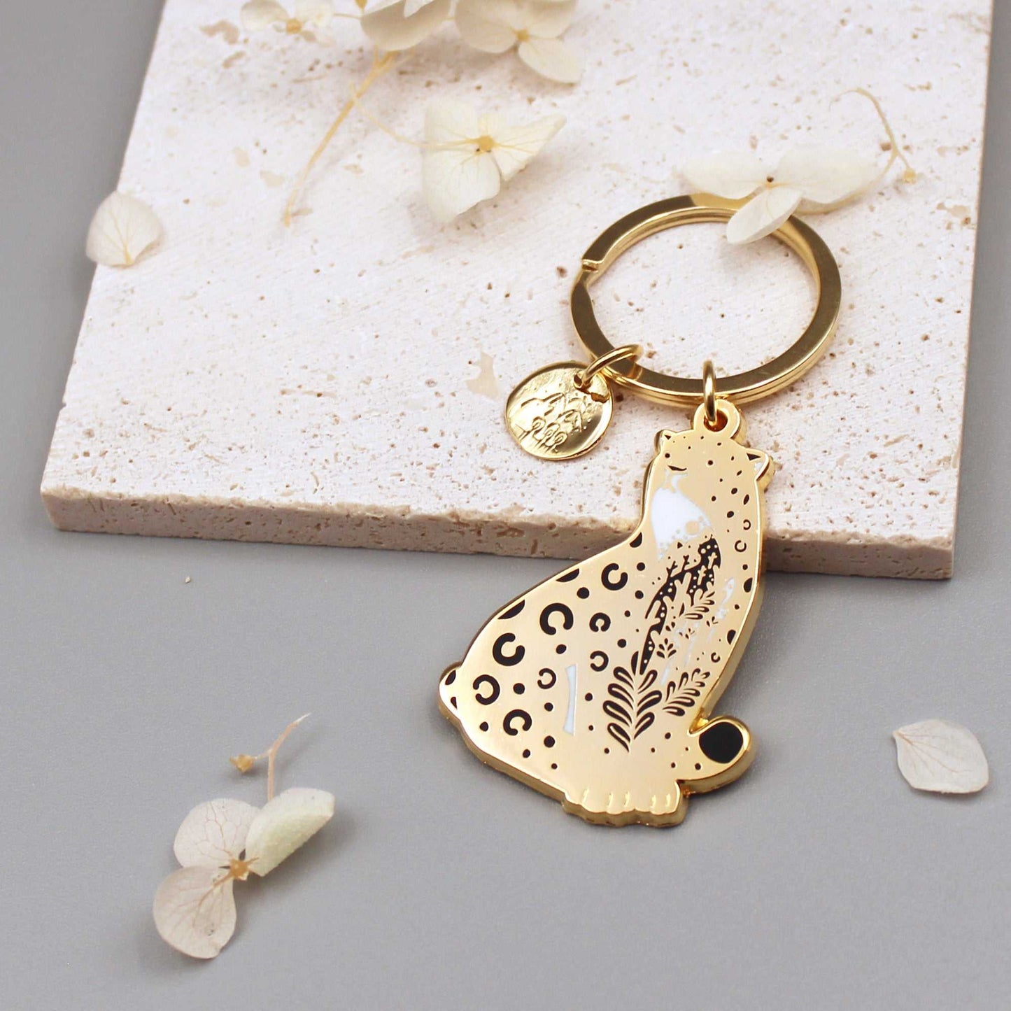 Amur Leopard enamel keychain with habitat design and gold charm on a stone background, promoting endangered animal awareness.