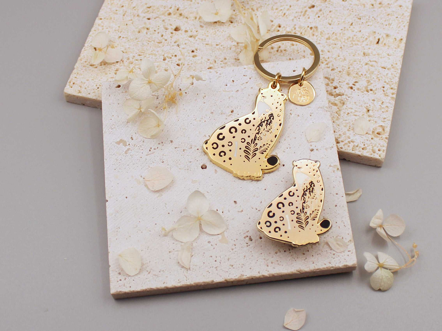 Amur leopard enamel keychain on a textured background, showcasing its delicate design and habitat illustration.