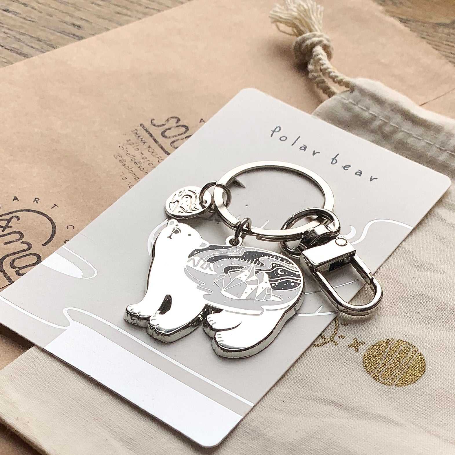 Polar bear enamel keychain with habitat illustration and round tag, emphasizing endangered wildlife conservation.