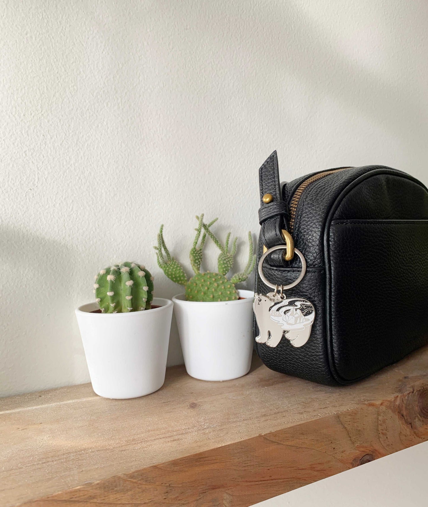 Black bag with Polar Bear keychain beside small potted cacti on wooden shelf.