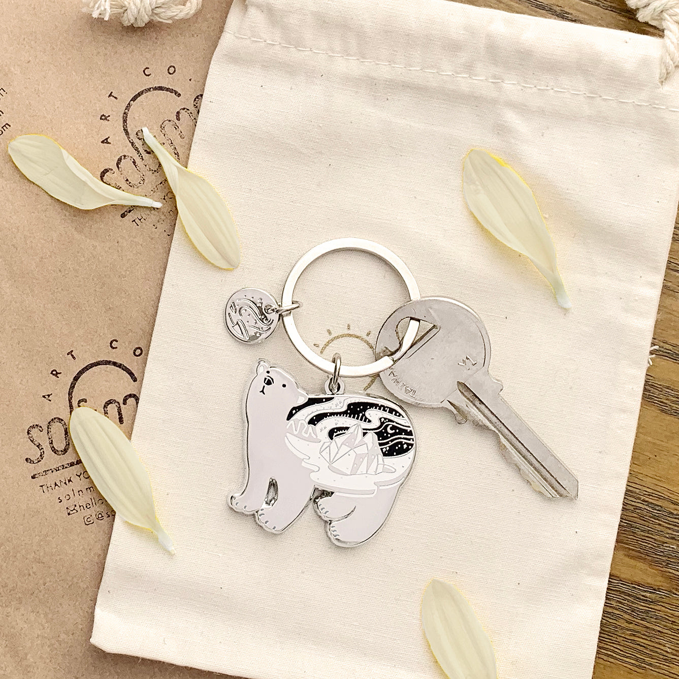 Polar bear enamel keychain featuring a delicate design and organic-shaped round tag, resting on a fabric pouch.