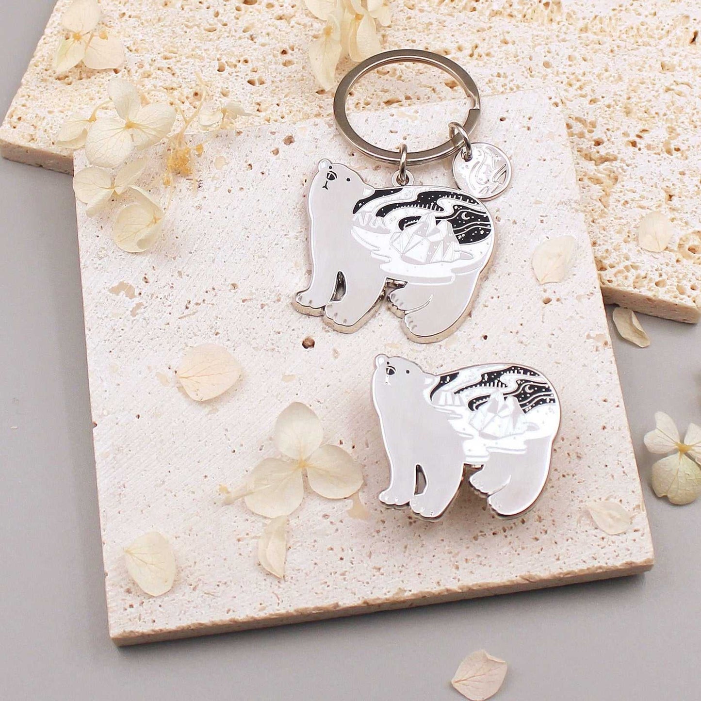 Polar Bear enamel keychain on a textured surface with floral details, showcasing delicate habitat art.