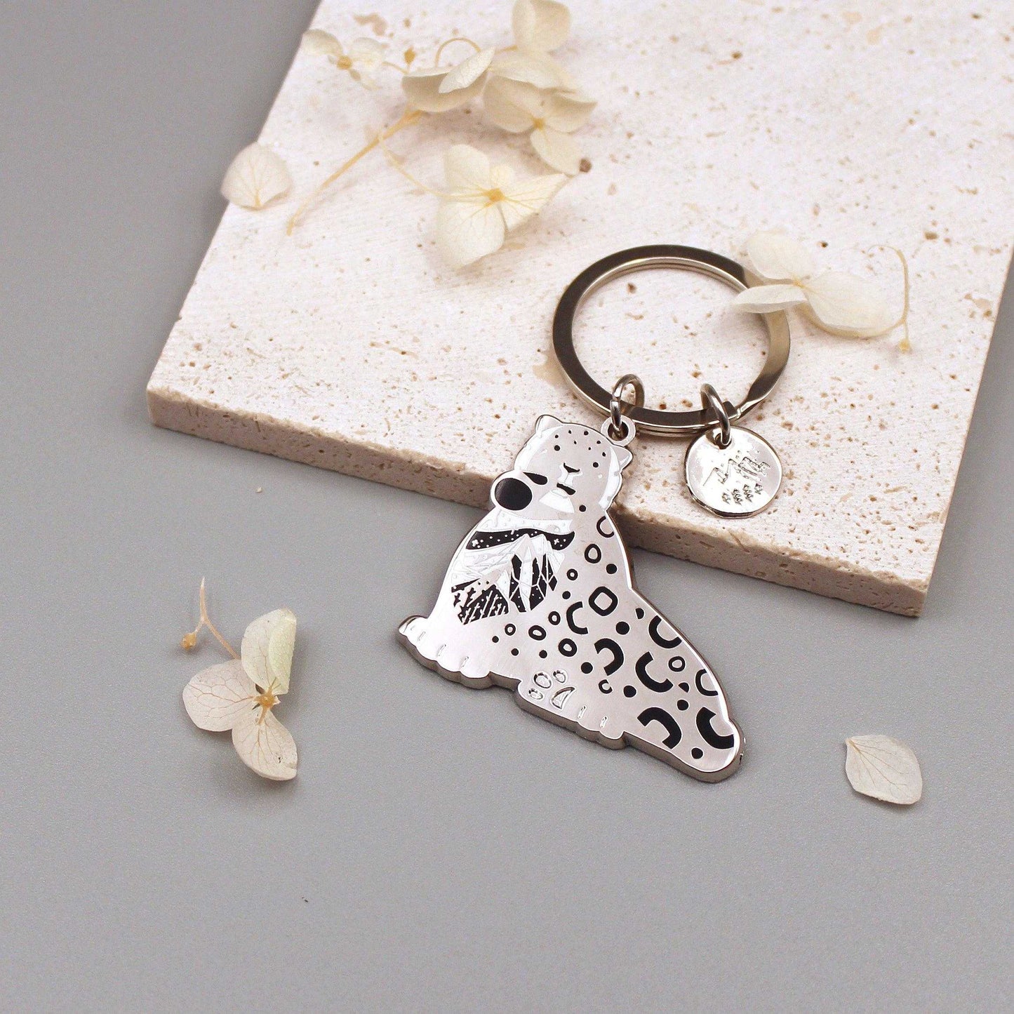 Snow Leopard enamel keychain featuring delicate art of its habitat on a round tag. Perfect for wildlife conservation advocates.