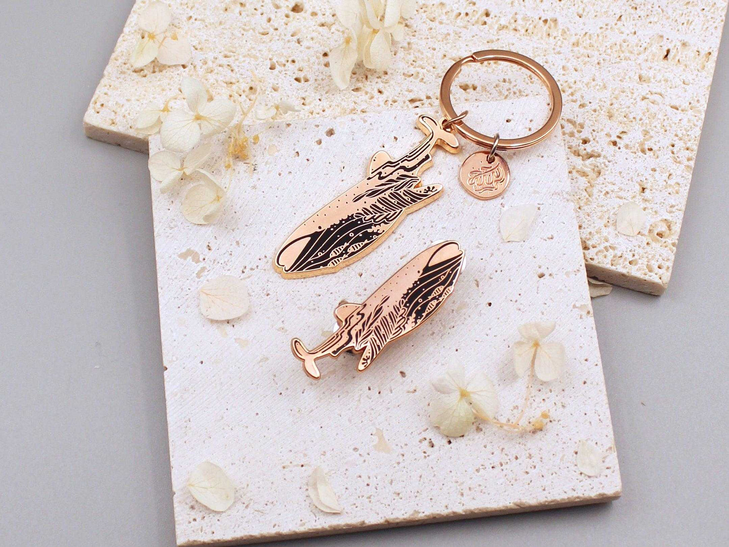 Whale Shark enamel keychain on a textured surface with floral accents, promoting endangered species awareness.