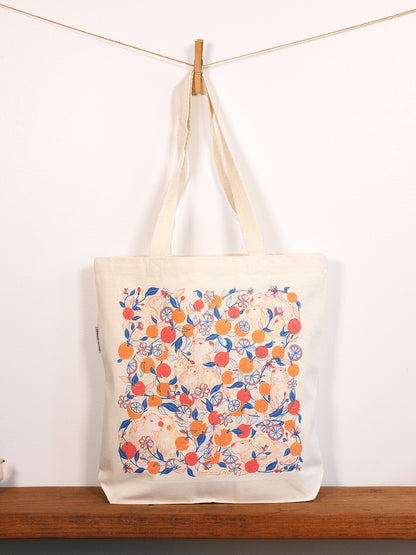 Tote bag with capybara & yuzu orange pattern hanging on a line against a white background