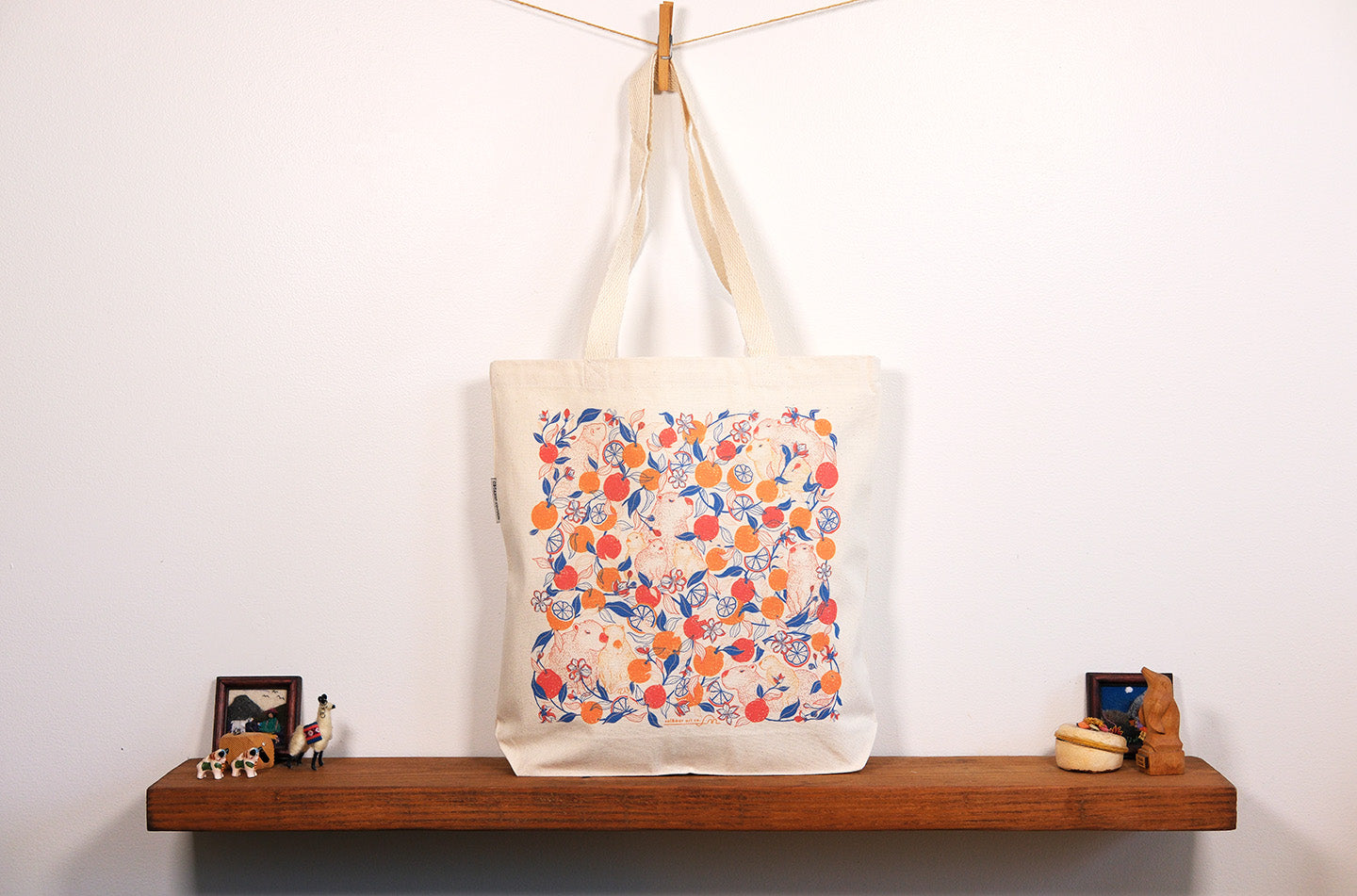 Tote bag with colorful capybara & yuzu orange  pattern hanging on a wooden shelf against a white wall