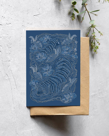 Blue greeting card with intricate design on a textured surface with greenery.