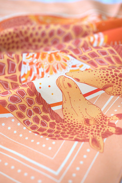 Close-up of a patterned silk scarf with giraffe design on an orange background