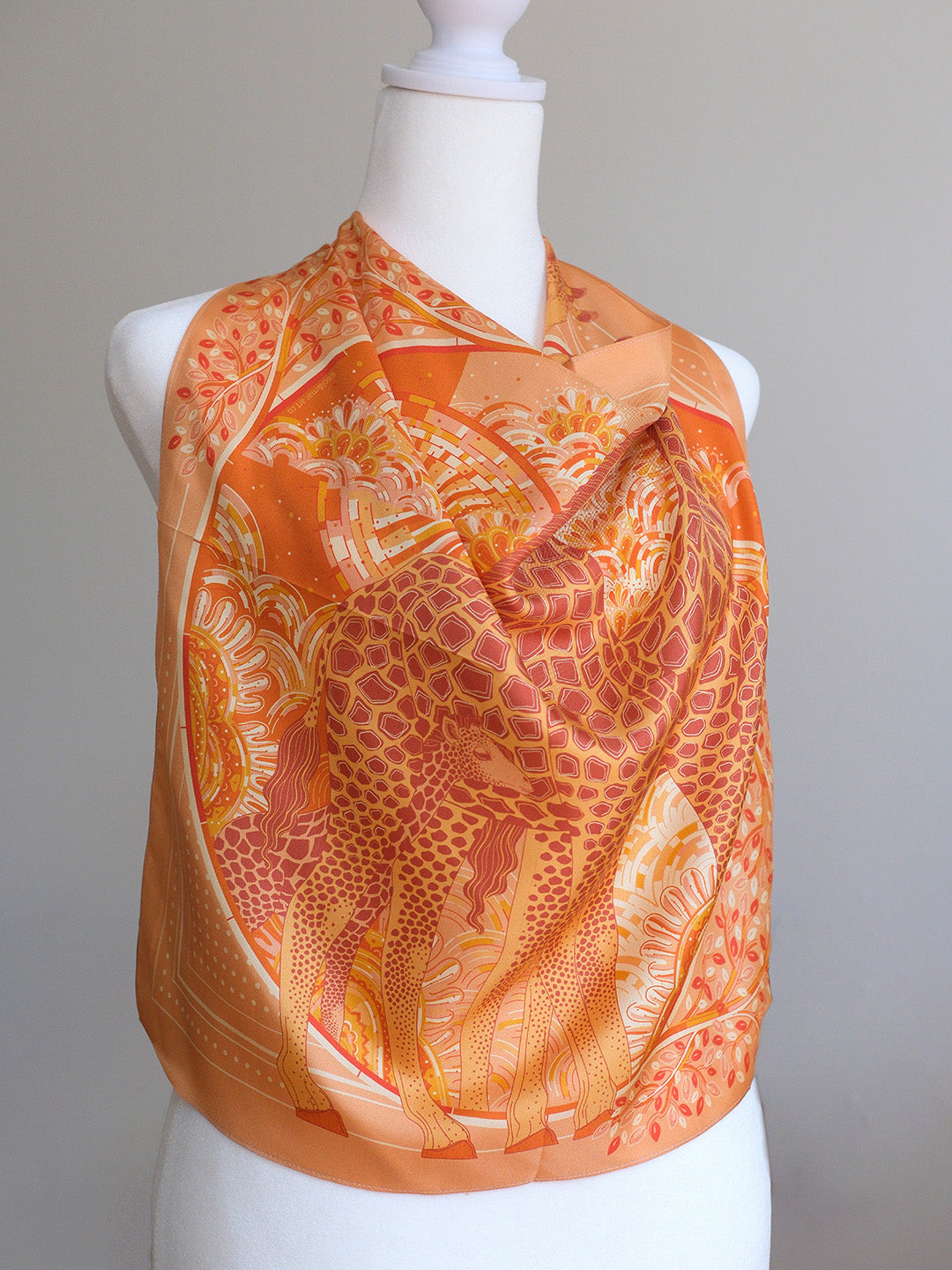 Orange giraffe patterned scarf on a mannequin against a gray background