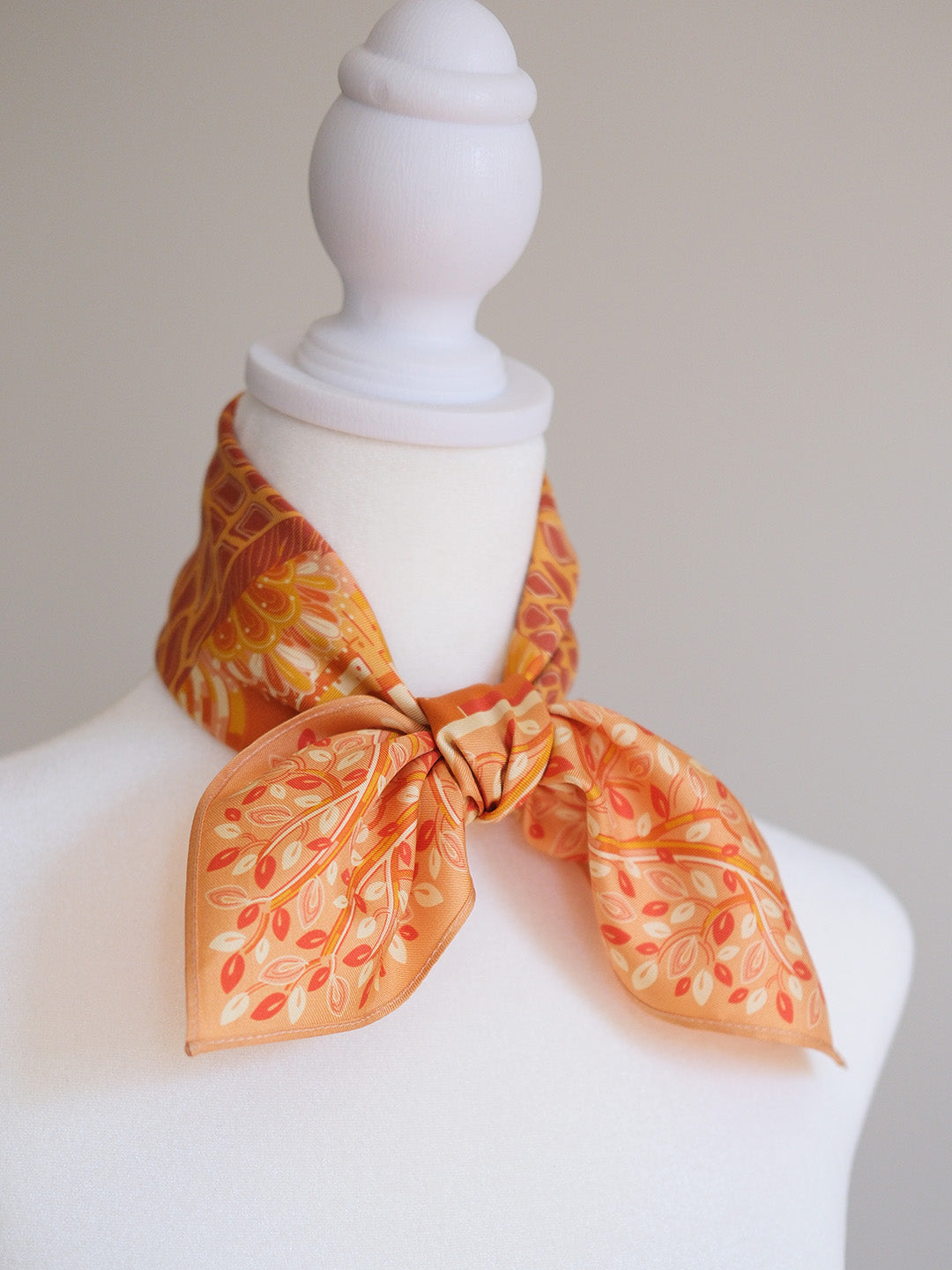 Mannequin wearing an orange scarf with leaf pattern on a plain background