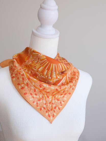 Orange scarf with leaf pattern on a mannequin against a plain background