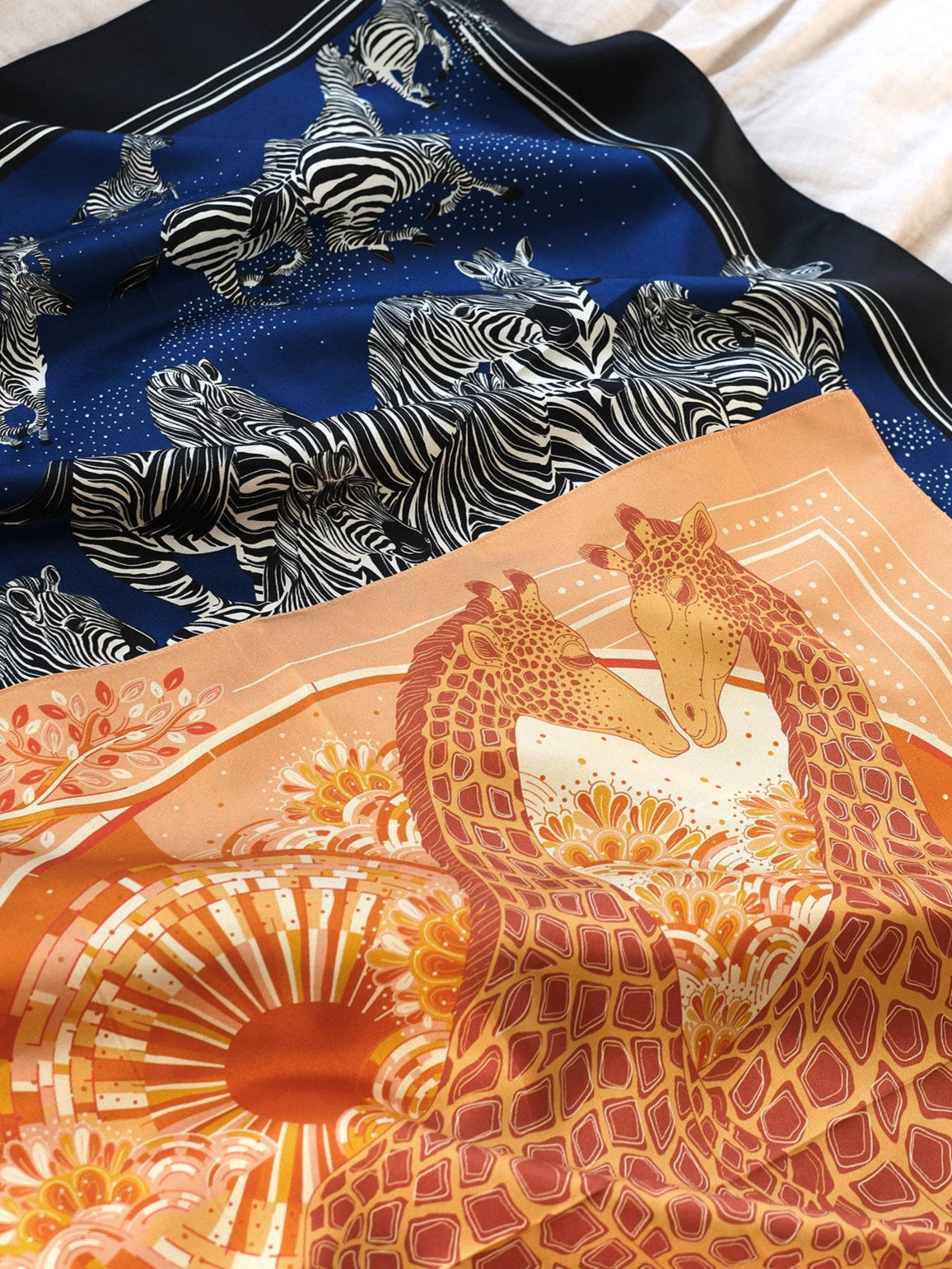 Two scarves with zebra and giraffe patterns on a textured surface.