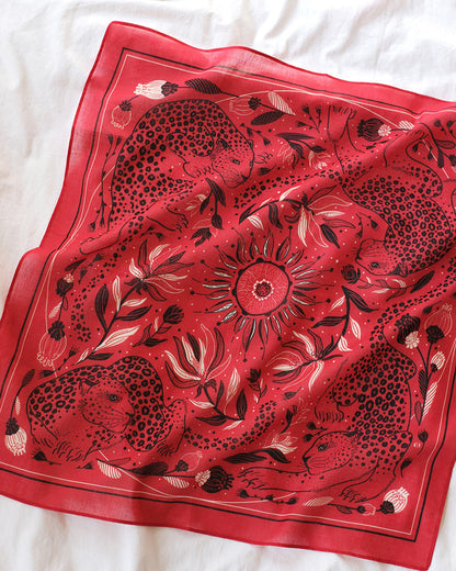 Red scarf with black floral and animal pattern on a white fabric background