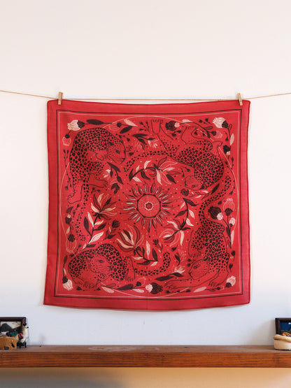 Red bandana with black and white patterns hanging on a line against a white wall.