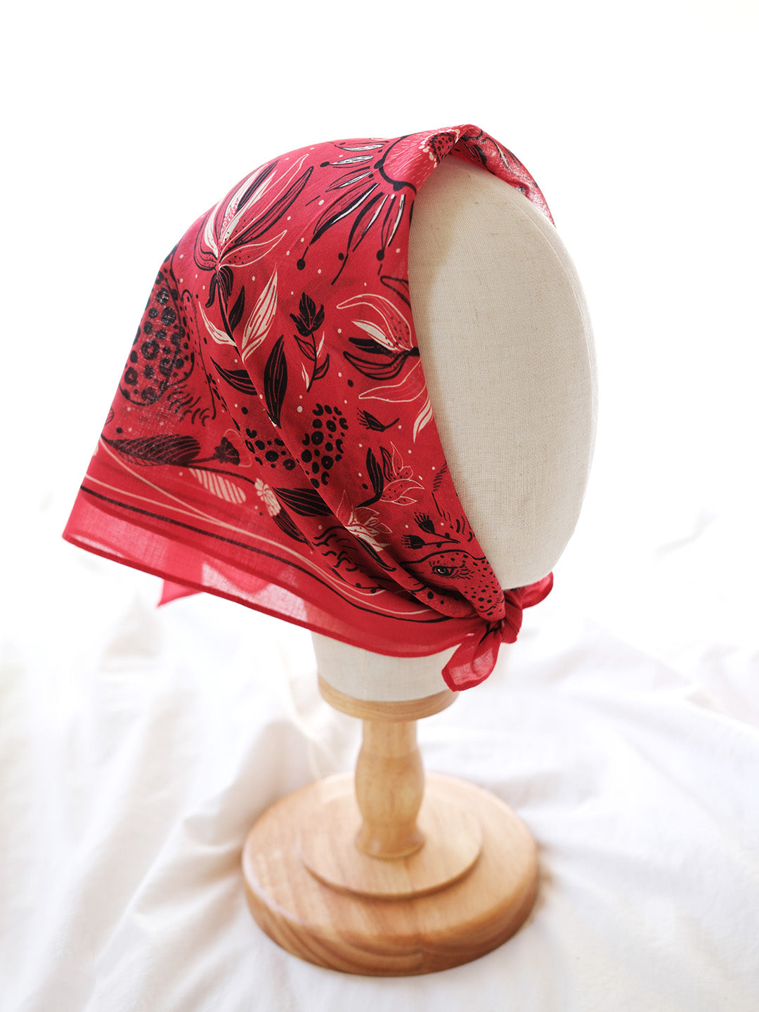 Red floral headscarf on a wooden mannequin head against a white background