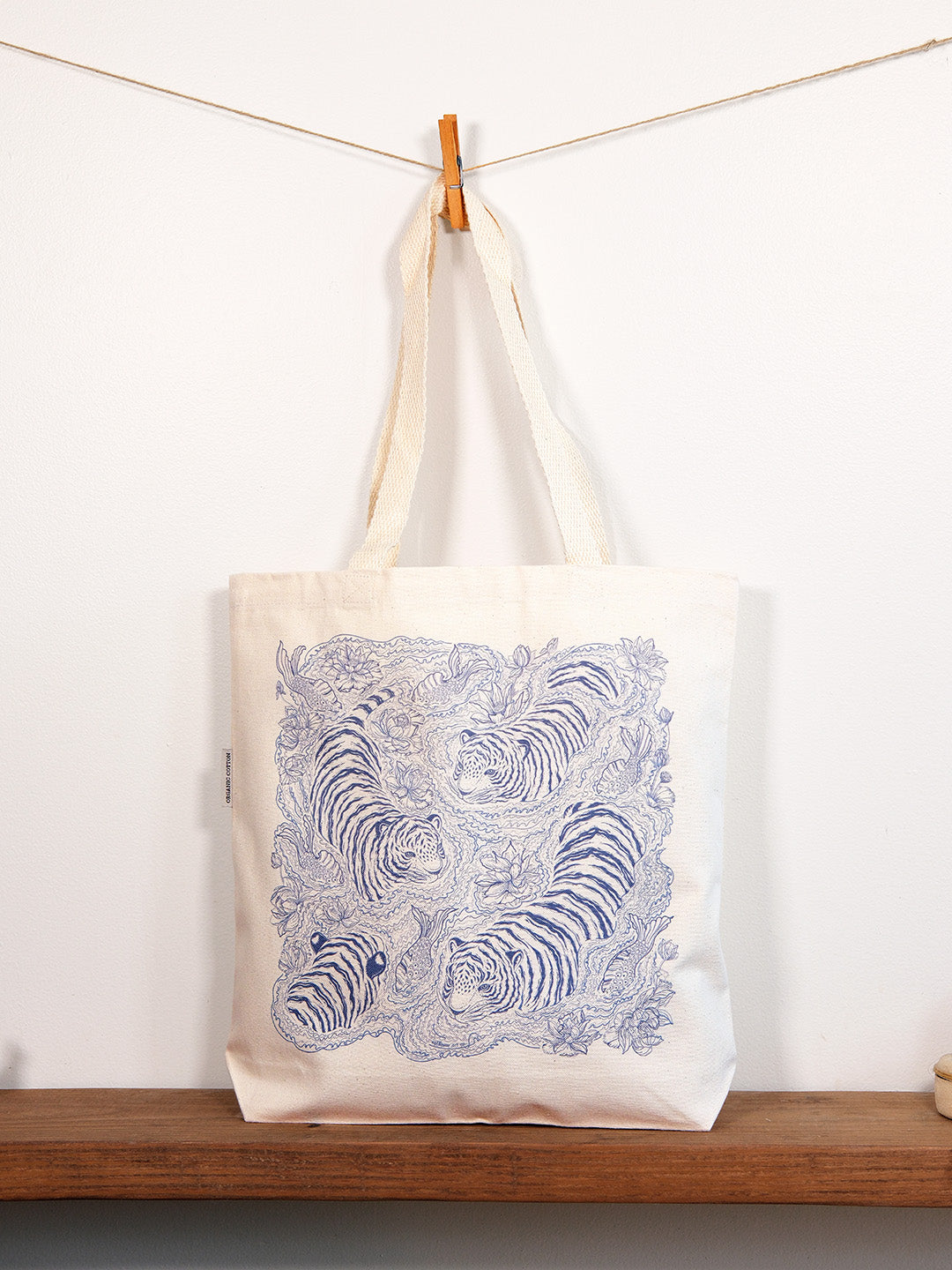 Tote bag with blue tiger design hanging on a clothesline against a white wall.