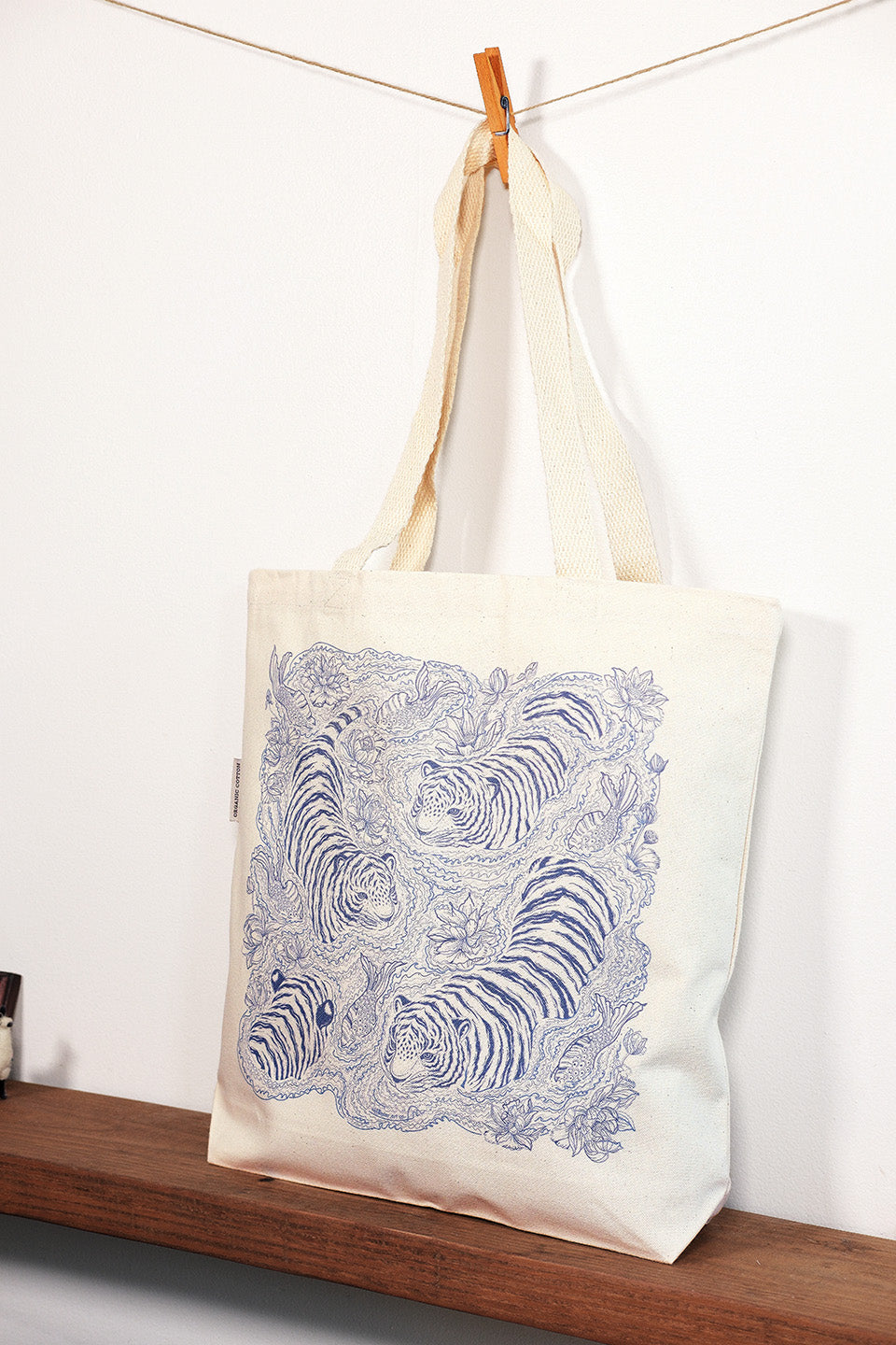Tote bag with blue tiger design hanging on a line against a white background