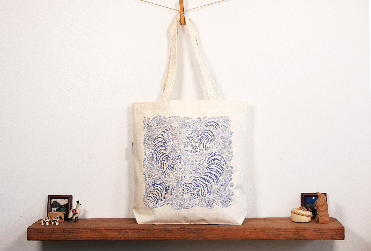 Tote bag with tiger pattern hanging on a hook against a white wall.