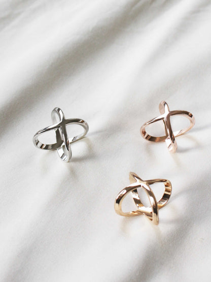Three stylish rings displayed on fabric: one silver, one rose gold, and one gold with a unique twisted design.