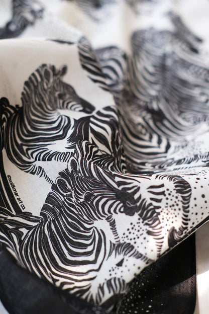 Close-up of a black and white bandana scarf featuring an artistic illustration of zebras.